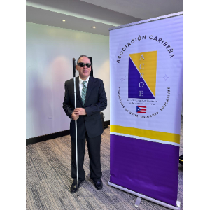 Foto de Manolo posando de pie junto al cartel de la conferencia ACPOE 2025.