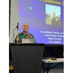 La foto muestra a Manolo ofreciendo su charla detrás de un podio.
