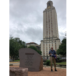 Foto de Manolo posando al lado de una torre alta con un reloj en la parte superior, que es el icónico edificio de la Universidad de Texas en Austin.