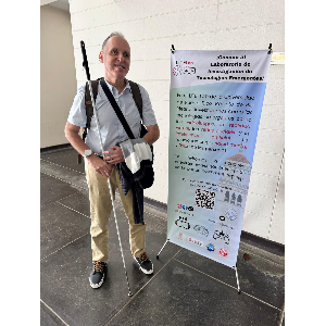 La foto presenta a Manolo de pie  al lado del cartel del congreso de videojuegos.