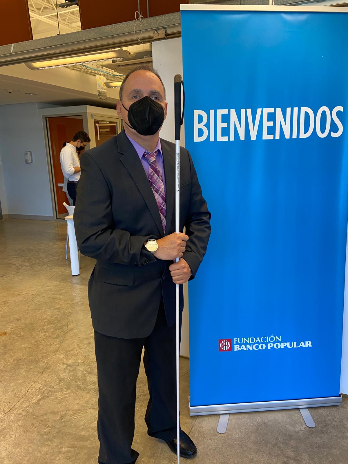 La foto muestra las facilidades donde se llevó a cabo la actividad de Talento de Sobra. La foto presenta a Manolo posando al lado del letrero de la Fundación del Banco Popular.
