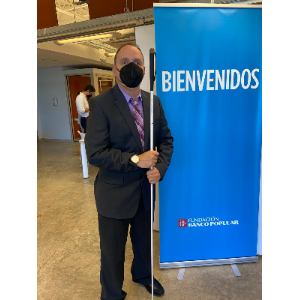 La foto presenta a Manolo posando al lado del letrero de la Fundación del Banco Popular.