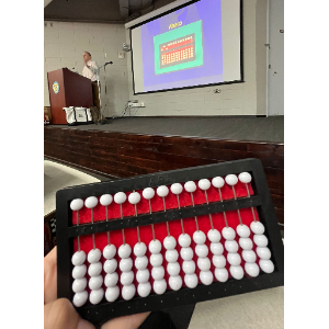 La foto presenta a Manolo en el podio de una tarima ofreciendo la charla relacionada a las matemáticas y los estudiantes ciegos.