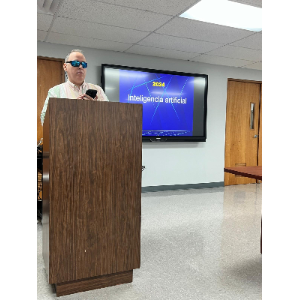 Foto de Manolo utilizando su computadora mientras ofrece la charla desde el podio.