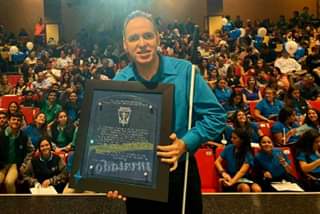 Los estudiantes se encuentran en la tarima del teatro. La foto muestra a Manolo posando junto a estudiantes de la Sociedad de Honor del Colegio Maristas en Guaynabo.