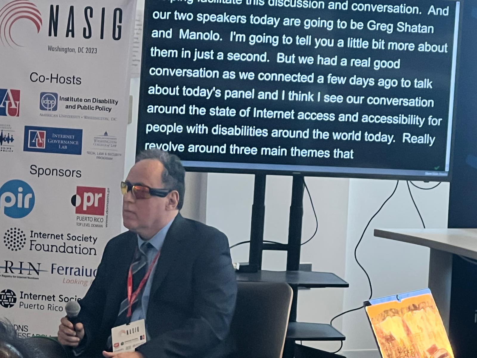 El letrero presenta la información de la conferencia en la American University en Washignton DC. La foto muestra a Manolo posando al lado del cartel de la Conferencia NASIG 2023.