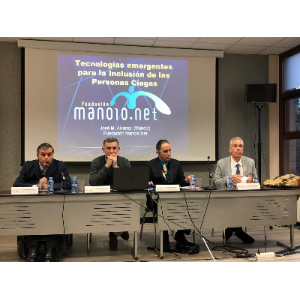 La foto muestra a cuatro hombres sentados detrás de una mesa durante la conferencia CIUD 2018 en España. Detrás de ellos hay una pantalla de proyección que muestra el título Tecnologías emergentes para la Inclusión de las Personas Ciegas.