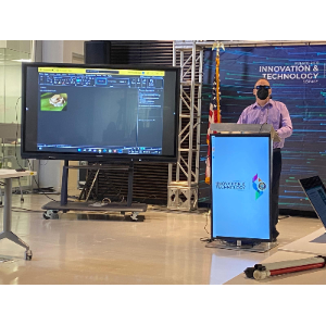 Foto de Manolo haciendo su presentación utilizando su computadora en el podio.