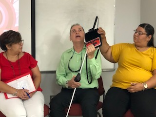 Los panelistas se encuentran sentados en la parte frontal del salón. La foto presenta a Manolo demostrando varias tecnologías como parte del panel.